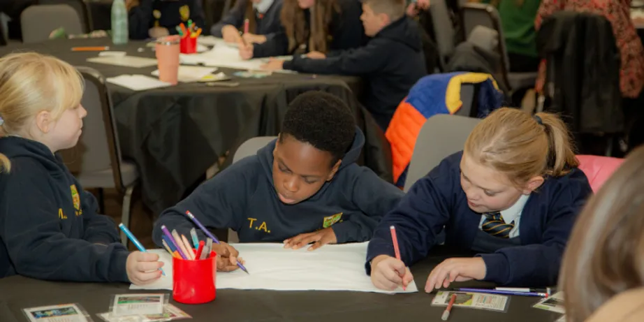 Three schoolboys in blue uniforms writing at a desk.