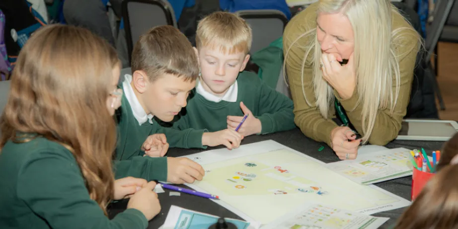 Schoolboys wearing green uniforms work at a desk with a female teacher