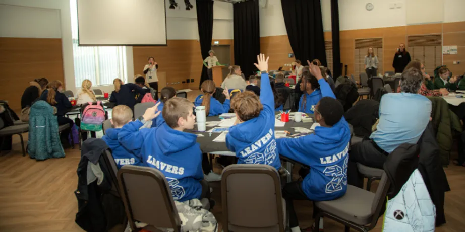 Schoolboys wearing a light blue uniform hold their hands up to speak.