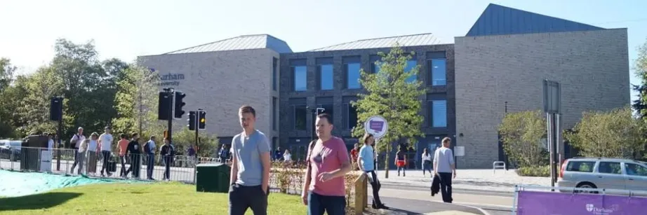 People walking in front of a large building with trees in front of it on a sunny day
