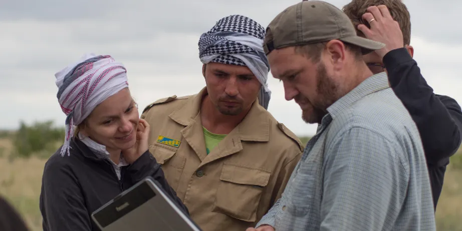 Three men and a woman all with headgear are looking at documents in the field