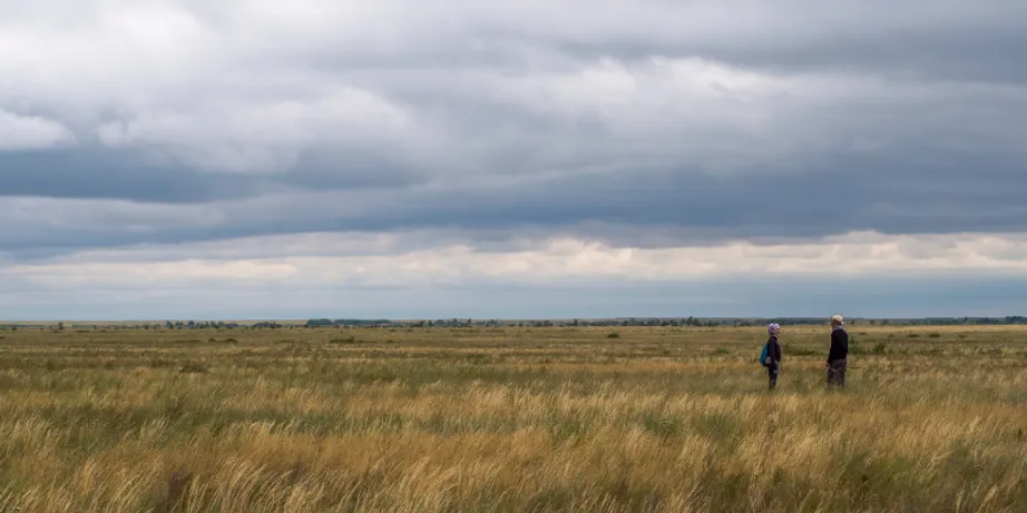 A man and a woman silhouetted against a grassland landscape with a cloudy sky above.