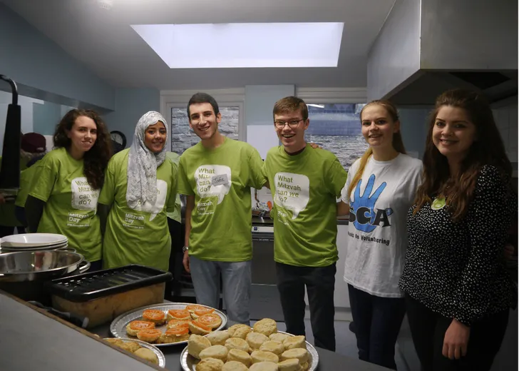 A large group of student behind a counter of food in a kitchen