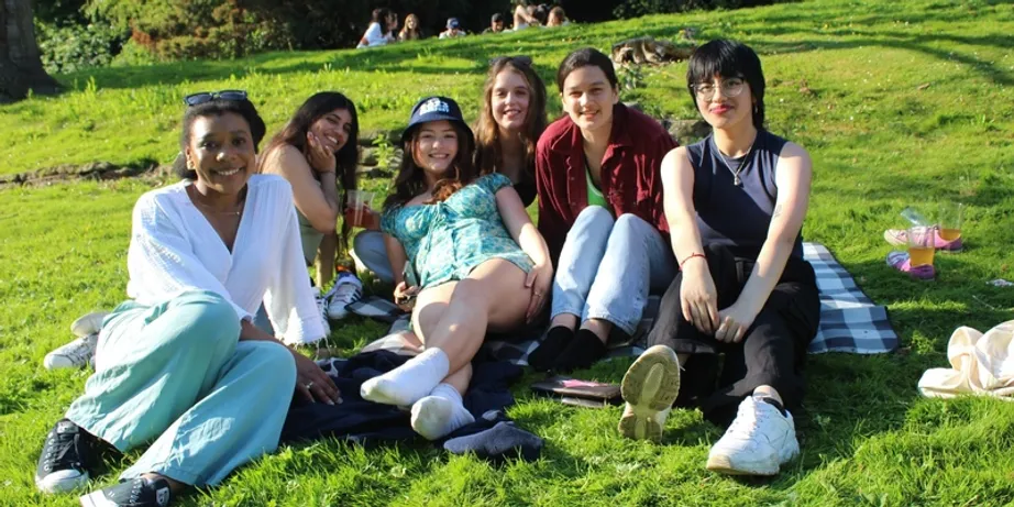 A group of six students sitting on a grass hill in the sunshine