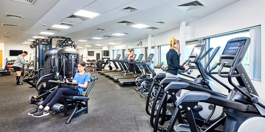 An image of a lot of gym equipment with people working out on various machines