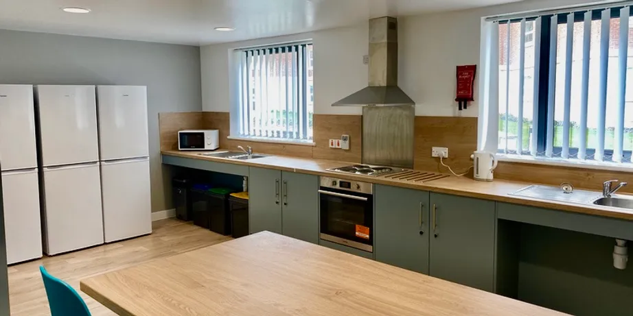 A picture of the inside of a town house kitchen. Shown are a large prep and cooking area, an oven and hob, and 3 refrigerators.