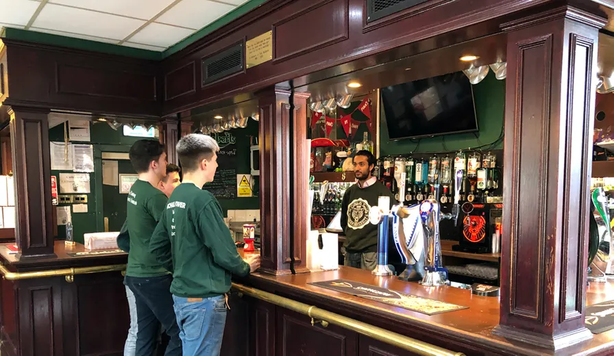 Traditional wooden bar with students ordering drinks.