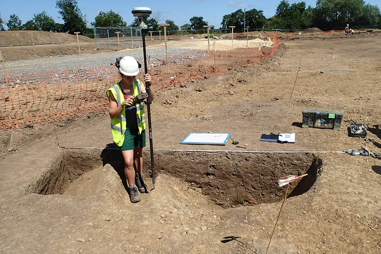 An archaeologist using a gps to record an excavated ditch section