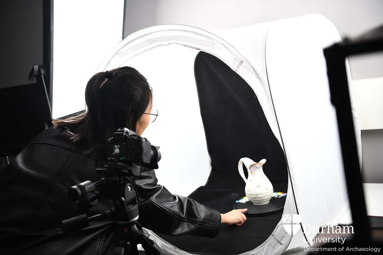 Student using camera and lightbox to photograph a ceramic jug