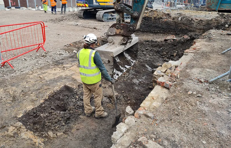 A person in high visibility clothing watching a JCB digging