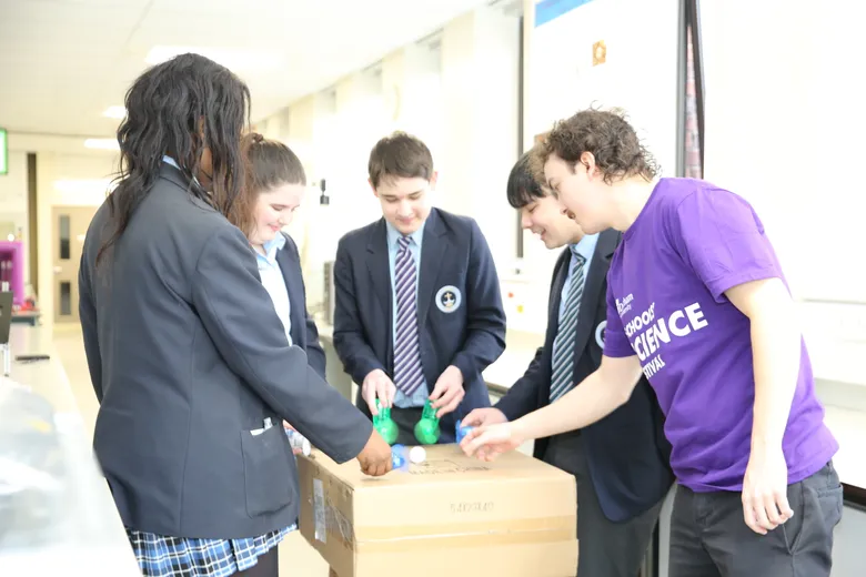 Group of four teensage students working with older tutor on desk based science experiment