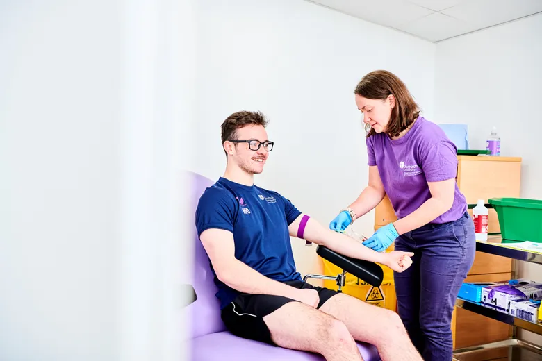 A student sitting in a phlebotomy chair having their blood taken for analysis by staff member