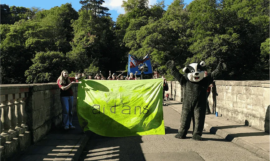 A student and a badger mascot with Aidans written on a neon yellow banner
