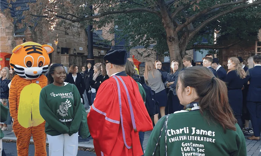 Students, staff and a tiger mascot outside with trees in the background