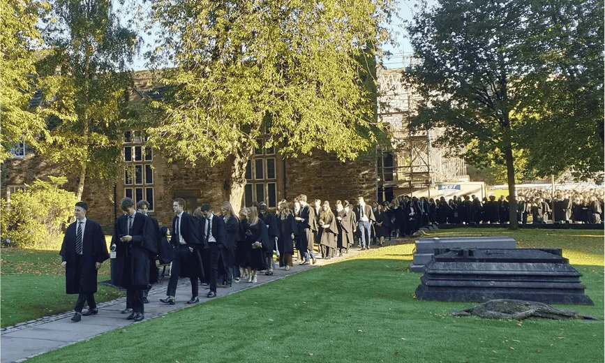 Students in robes walking on a path with trees in the background