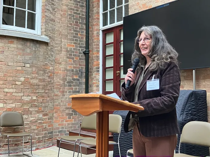 A lady at a lectern with a microphone speaking to an unseen audience