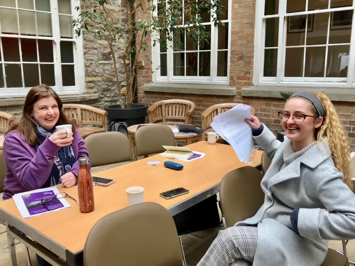 Two people sitting across a table looking up from a conversation to smile at the camera