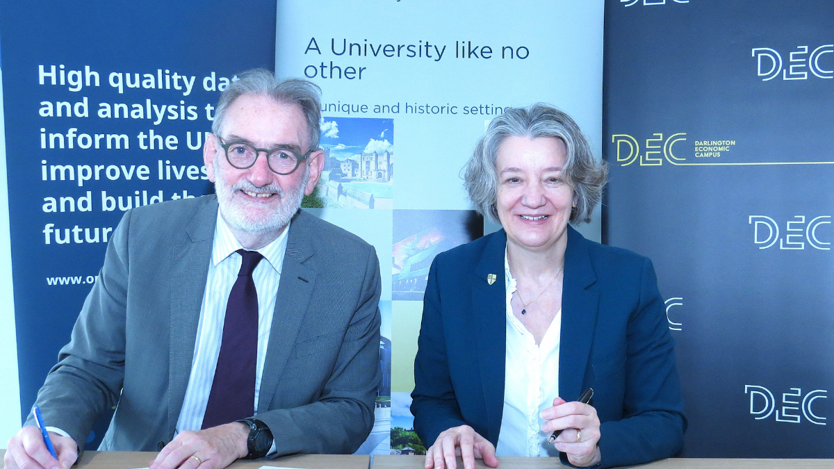 Sir Ian Diamond, National Statistician, and Professor Karen O’Brien, Vice-Chancellor and Warden in front of signs, signing an memorandum of understanding