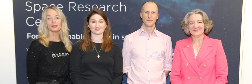 A group of people stand in front of a banner saying space research and smile at the camera.