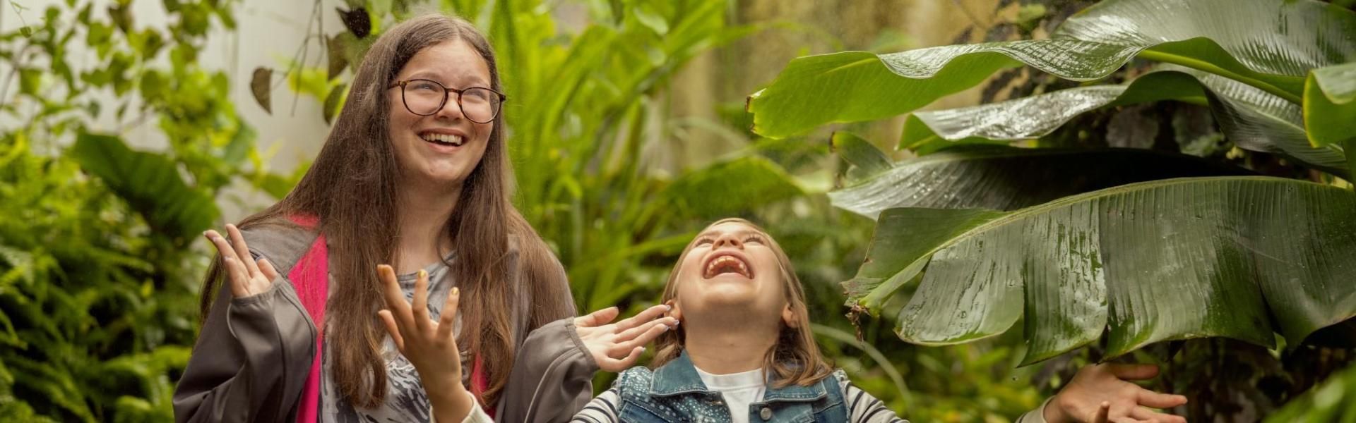 Two children enjoying the artificial rain in the Botanic Garden Greenhouse.