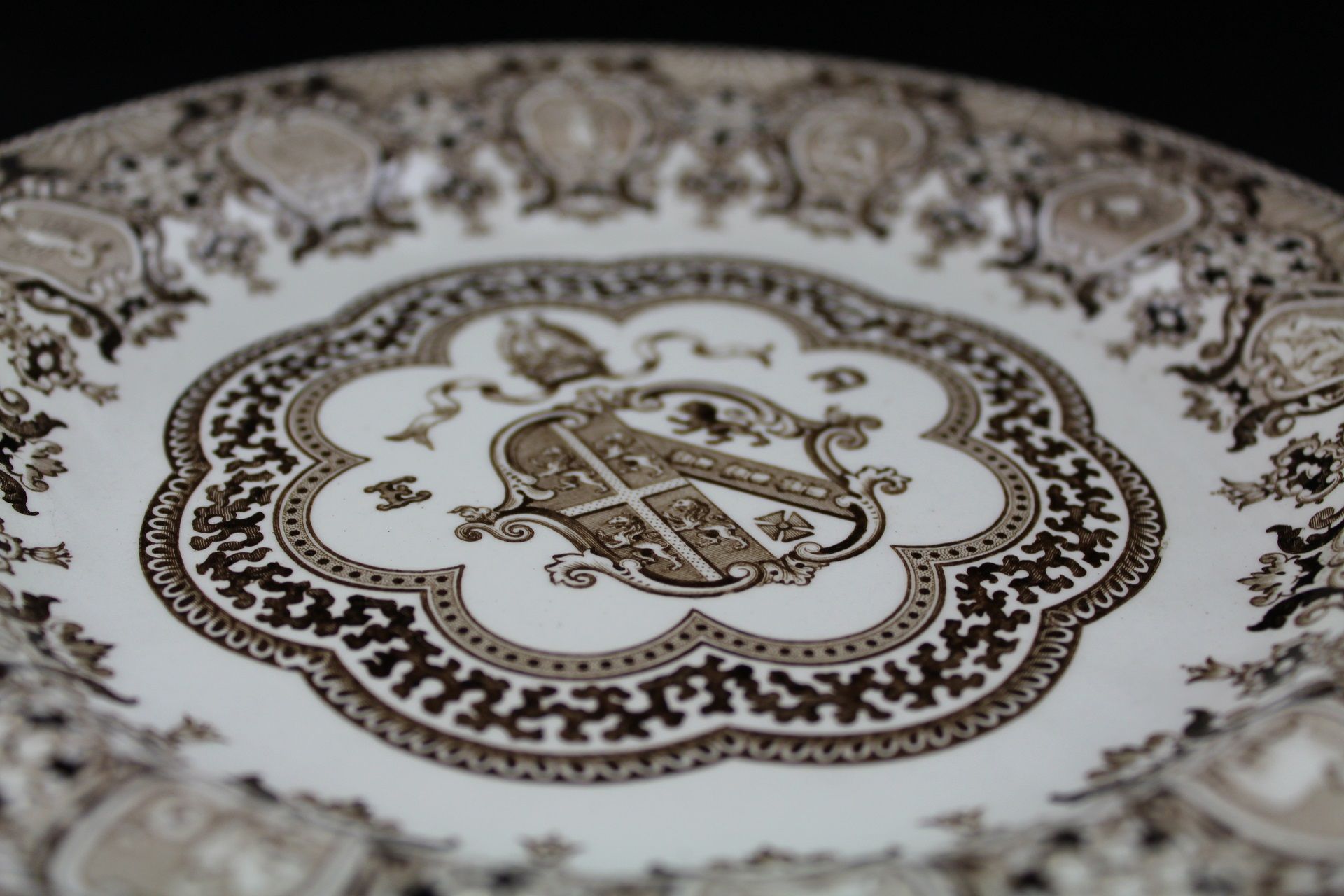 A coloured photograph showing the close-up detail on the plate, it includes the coat of arms for the Bishop of Durham at the centre. It is surrounded by scalloped floral detail and along the edge signs of the zodiac.