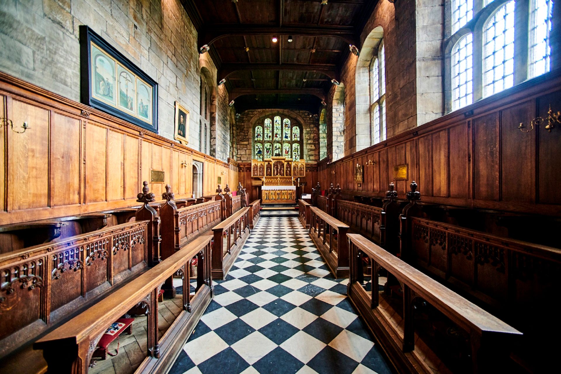 Photograph of the Tunstall Chapel and the stained glass at Durham Castle, at the centre is the altar and stained glass. At the sides are the pews and panelled walls.