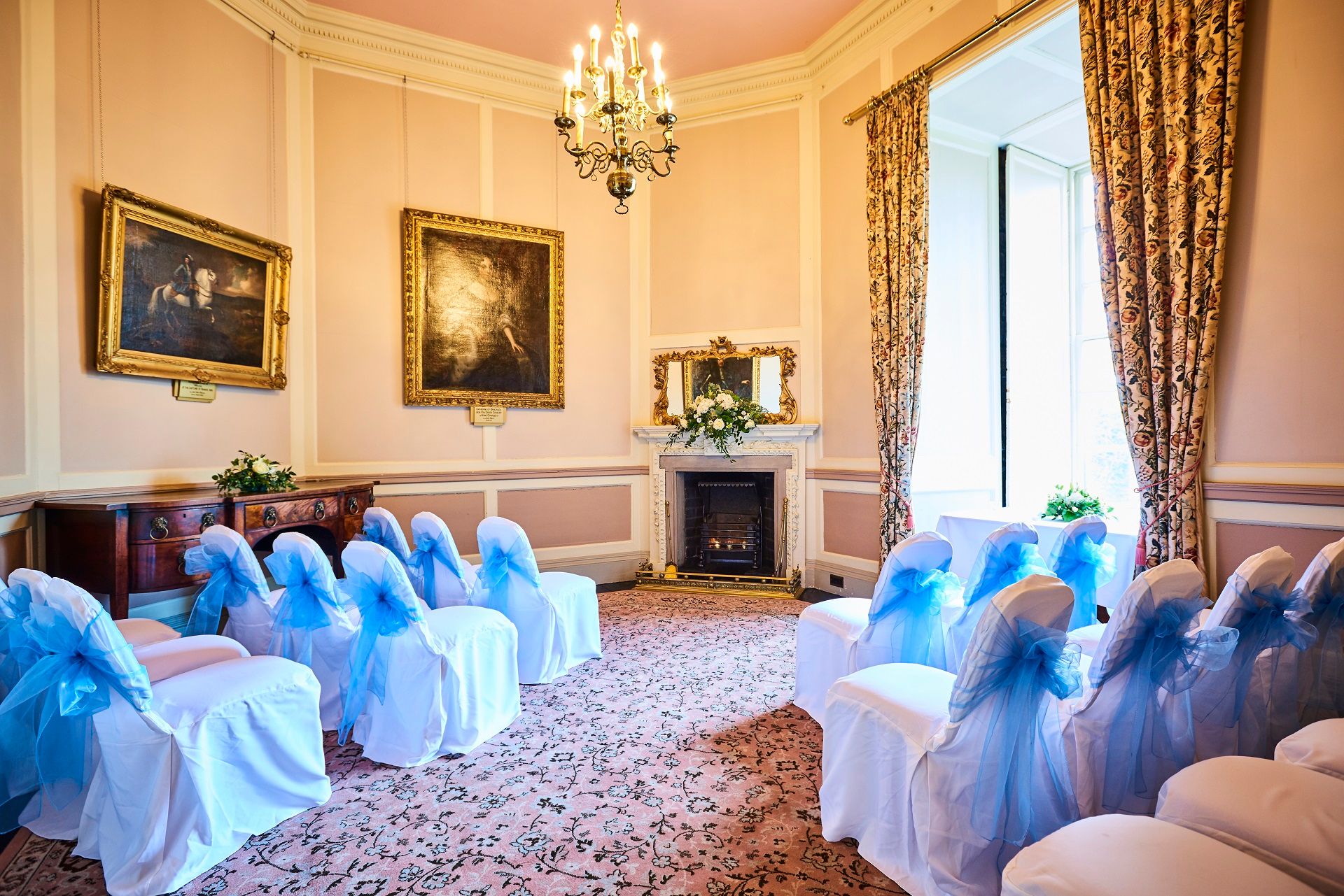 A coloured photograph showing the Octagon Room from the doorway. At the centre of the room is a fireplace, on the pink walls you can see a number of paintings.