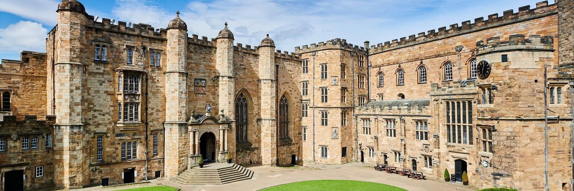 High stone buildings on two sides of a courtyard with a circular lawn in the centre and smaller areas of lawn against the sides.