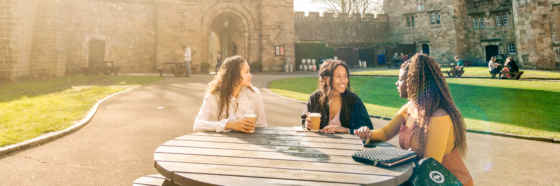 students sit in a group of 3 sipping coffee in the courtyard of university college