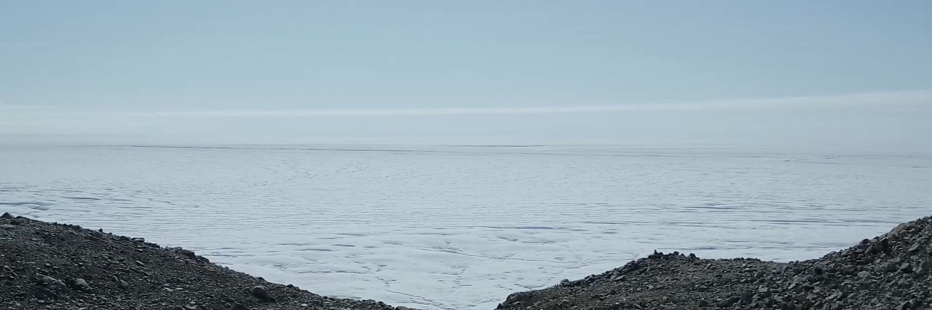 A panoramic view of an ice sheet with a rocky foreground