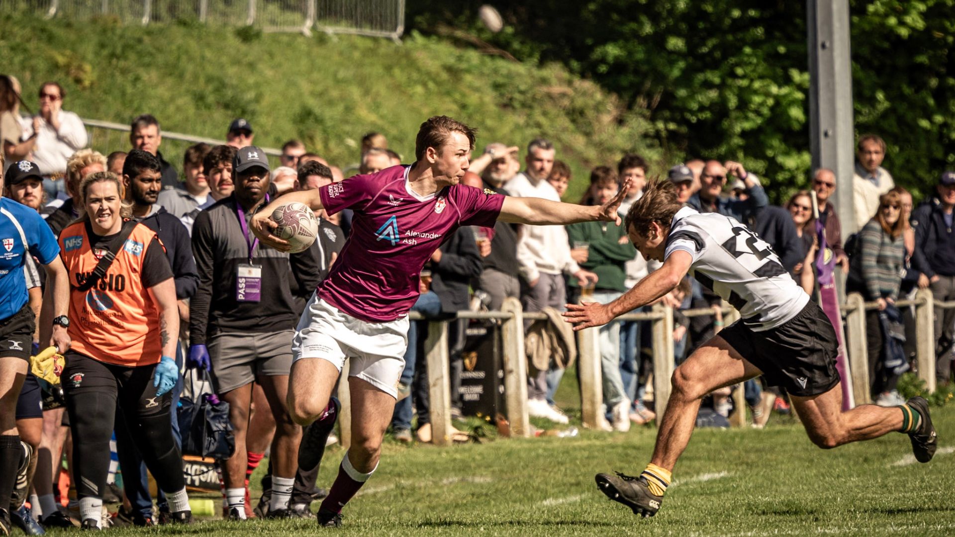 Two teams of rugby players wearing purple tops, and black and white tops, playing against each other