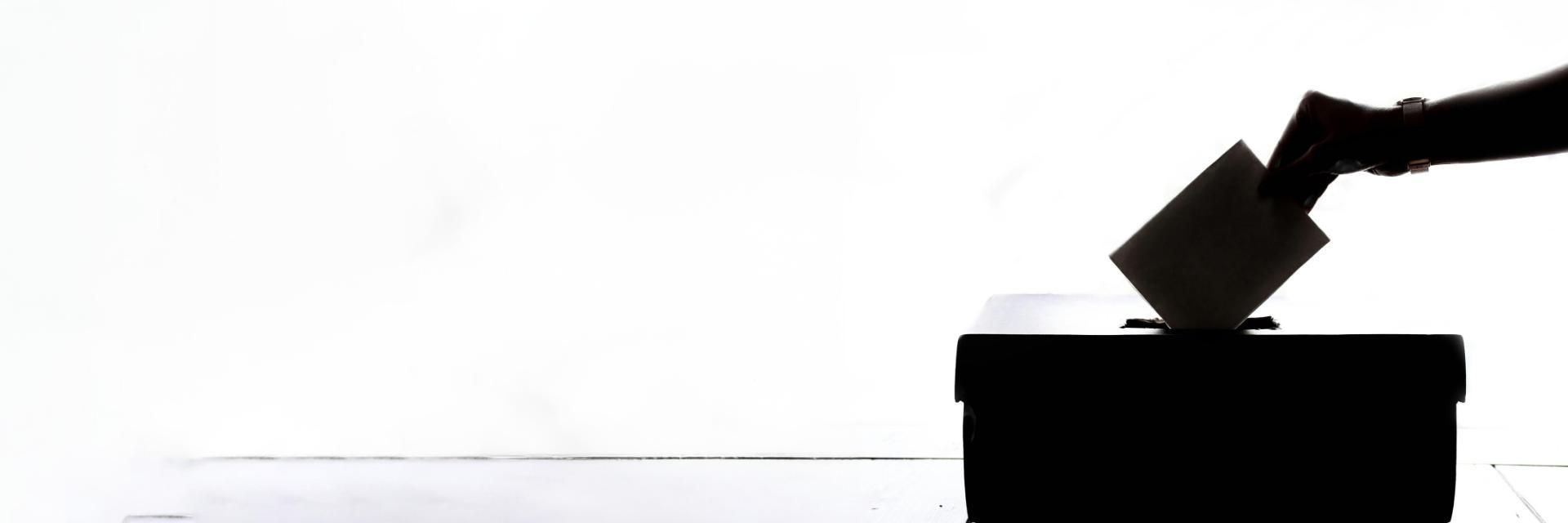 Silhouette of hand putting paper into ballot box