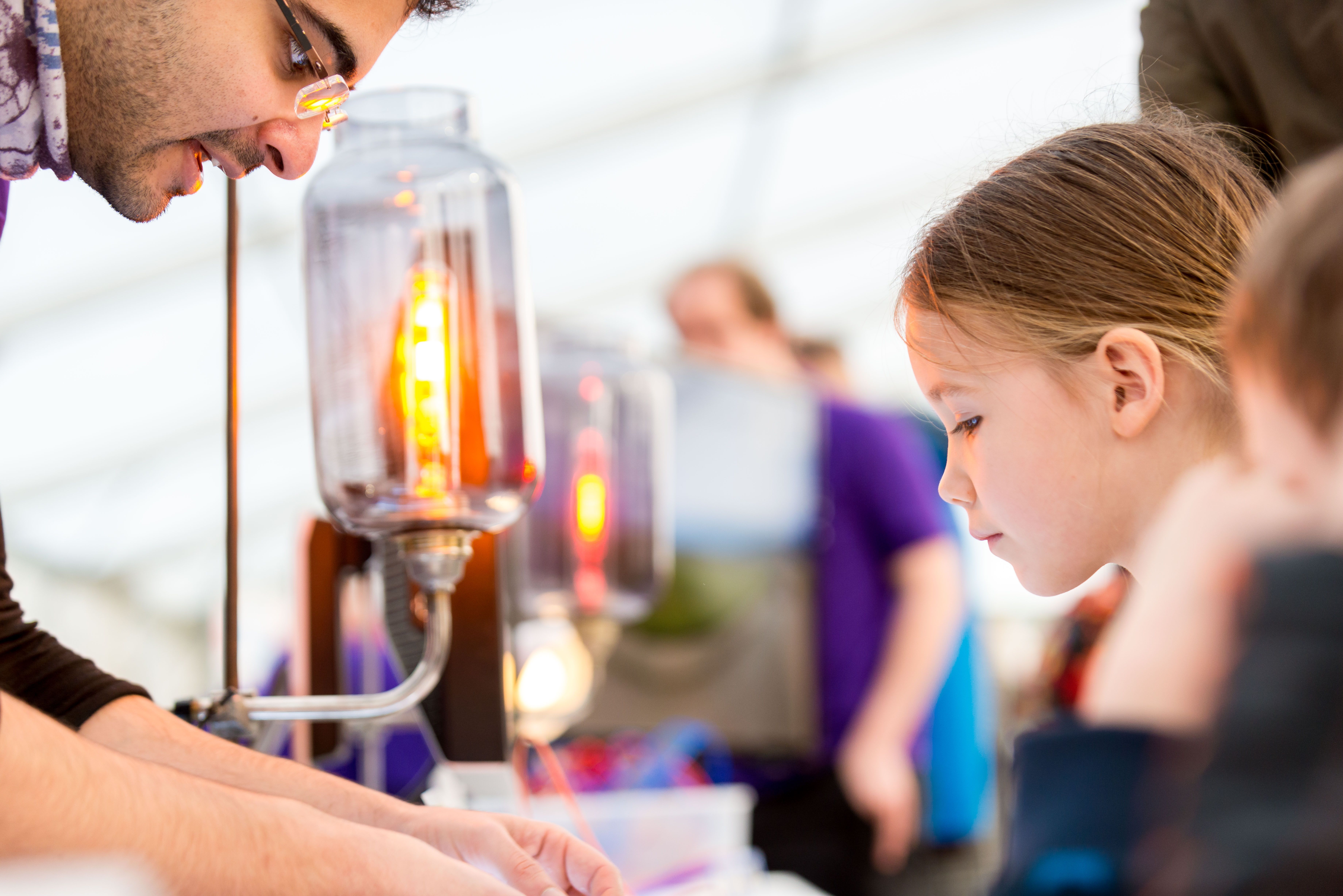 A young girl examining a science experiment, with a man leaning over to help her