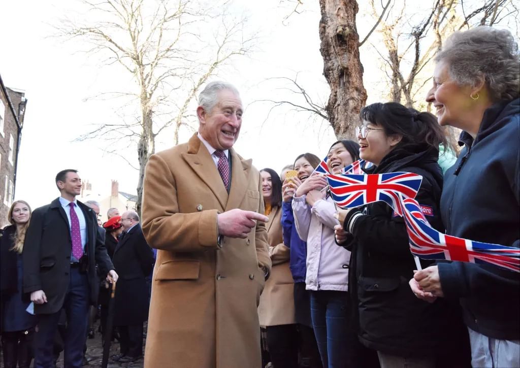 A man in a brown coat greets crowds waving Union flags