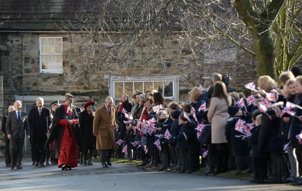 A man in a brown coat greets crowds lining a road