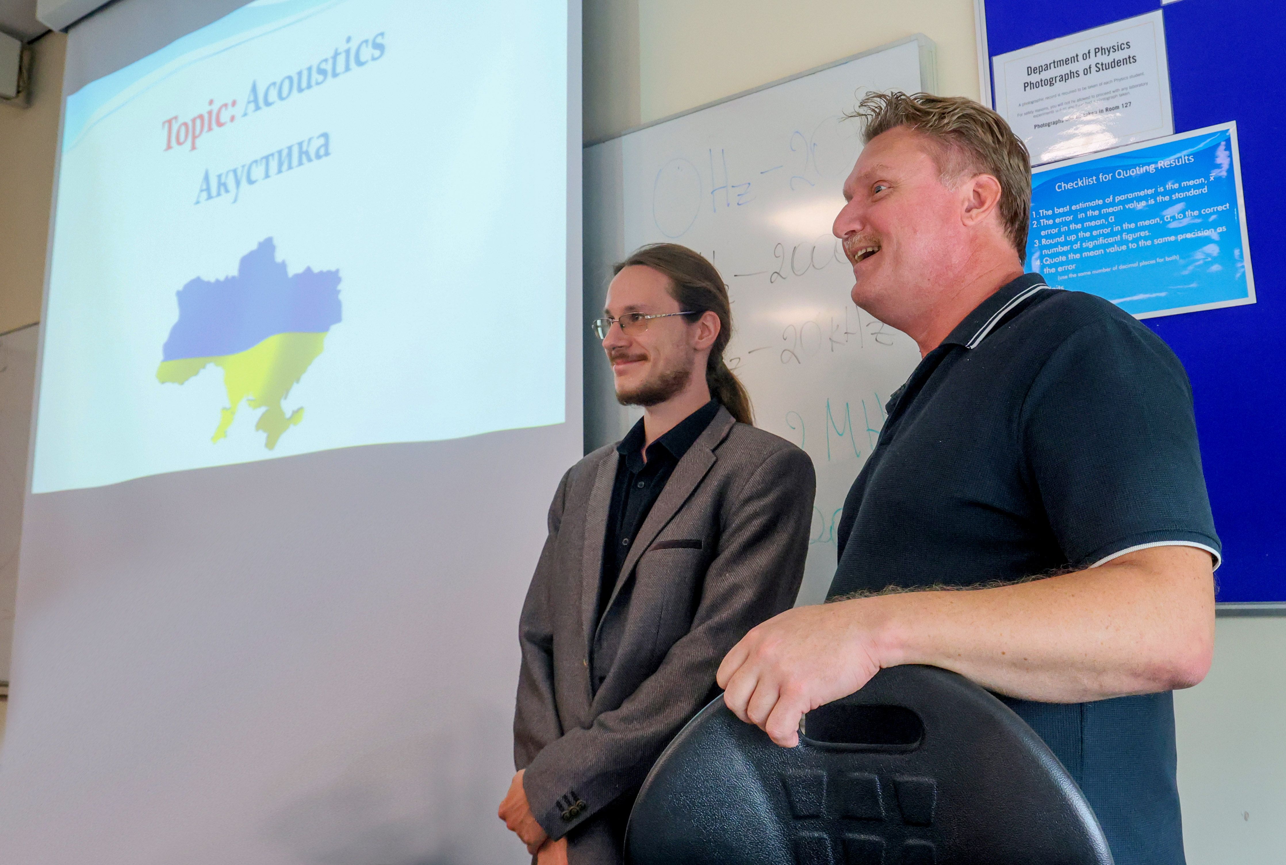 Two men standing in front of a projector screen displaying the Ukrainian flag