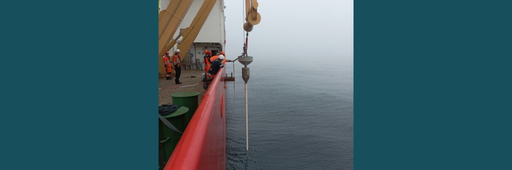 A pipe being lowered over the side of a ship into the sea to take sediment samples.