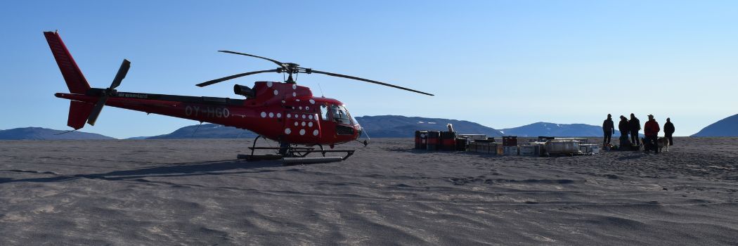 A helicopter and a team of scientists standing on an ice sheet and silhouetted against a blue sky.