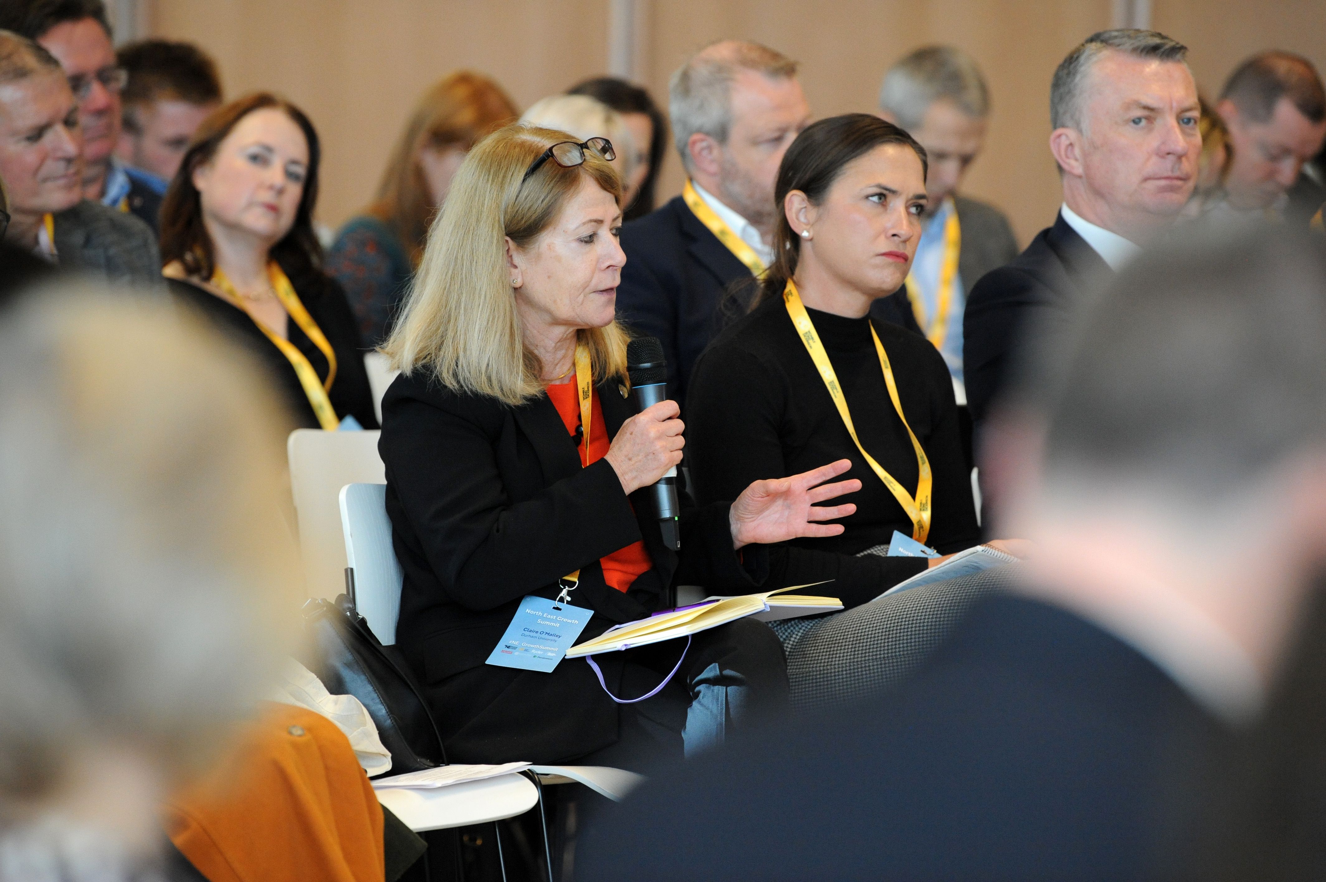 Woman speaking into microphone, seated, others listening