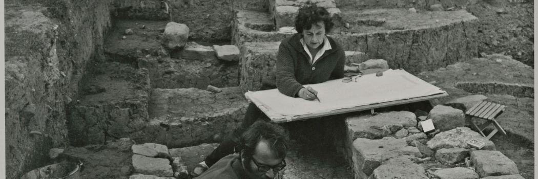 Black and white picture of Professor Dame Rosemary Cramp sketching during an archaeological dig