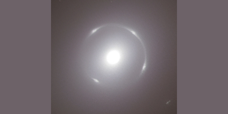 A close-up view of the centre of the bright, circular NGC 6505 galaxy, with the bright white Einstein Ring around its nucleus.