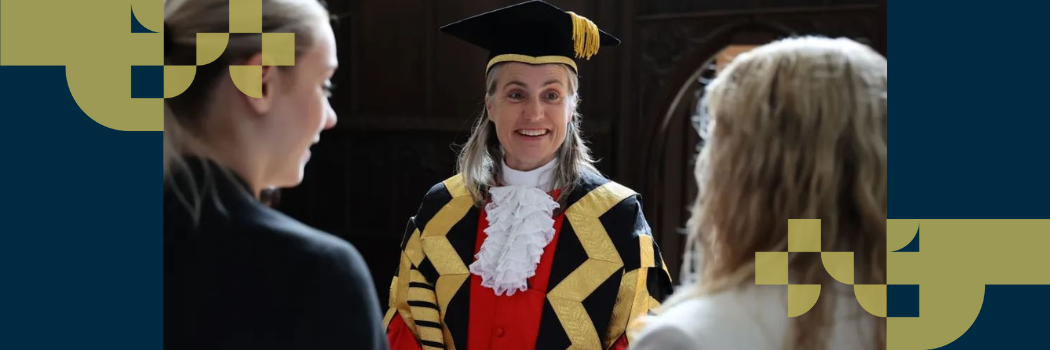 Fiona Hill wearing an academic gown smiling as she talks to two female students with their back to the camera