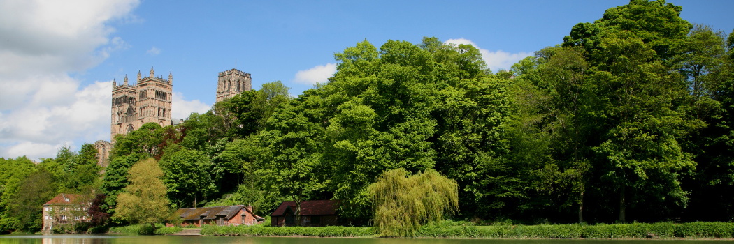 Durham Cathedral pictured on a sunny day with its reflection visible in the water.