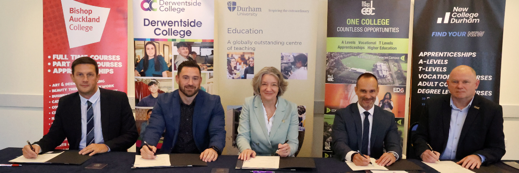 Five people signing a document at a table smiling