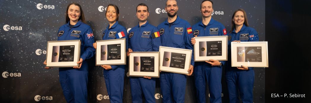 Astronaut graduates wearing blue boiler suits and holding their framed graduation certificates