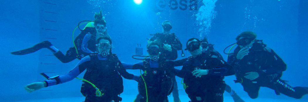 A group of scuba divers under water in a swimming pool looking at the camera.