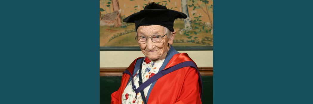 Margaret Bradshaw wearing a black academic cap and red robes smiling at the camera.