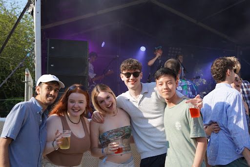 A group of students posing in front of an outdoor stage where a band is playing live music