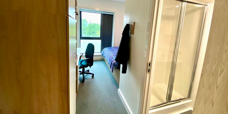 A picture of an en-suite room taken from the entrance. Pictured are a desk and chair, and a doorway to a toilet and shower.