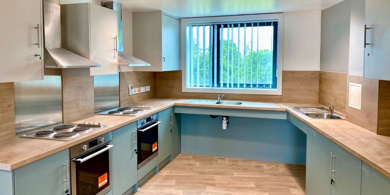 Pictured is one of our cluster flat kitchens for 8 en-suite rooms. Shown are a large sink, 2 ovens and 2 sets of hobs. There is also a window that shows trees across from the kitchen.